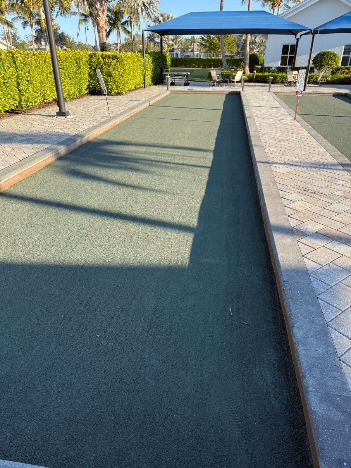 Bocce ball court with blue shade structure and paved surroundings in residential community