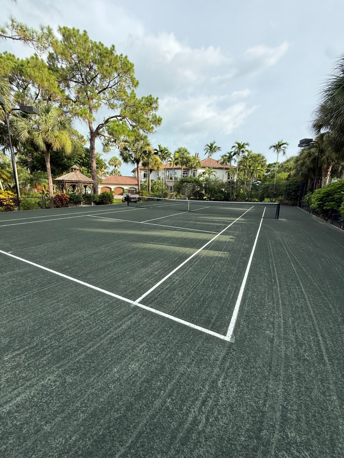 Professional tennis court with white lines and net in tropical estate setting
