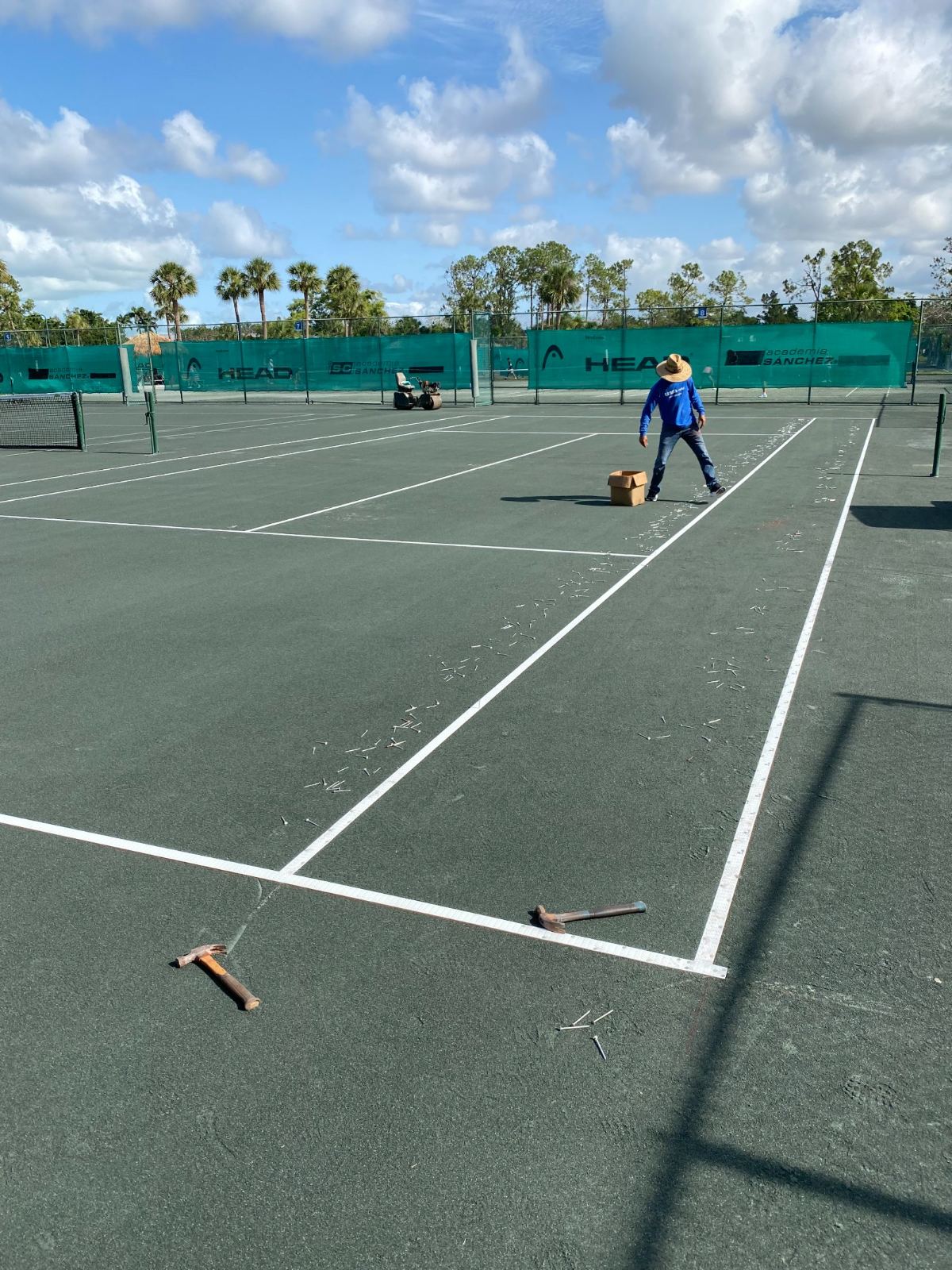 Tennis court maintenance worker clearing debris from court surface