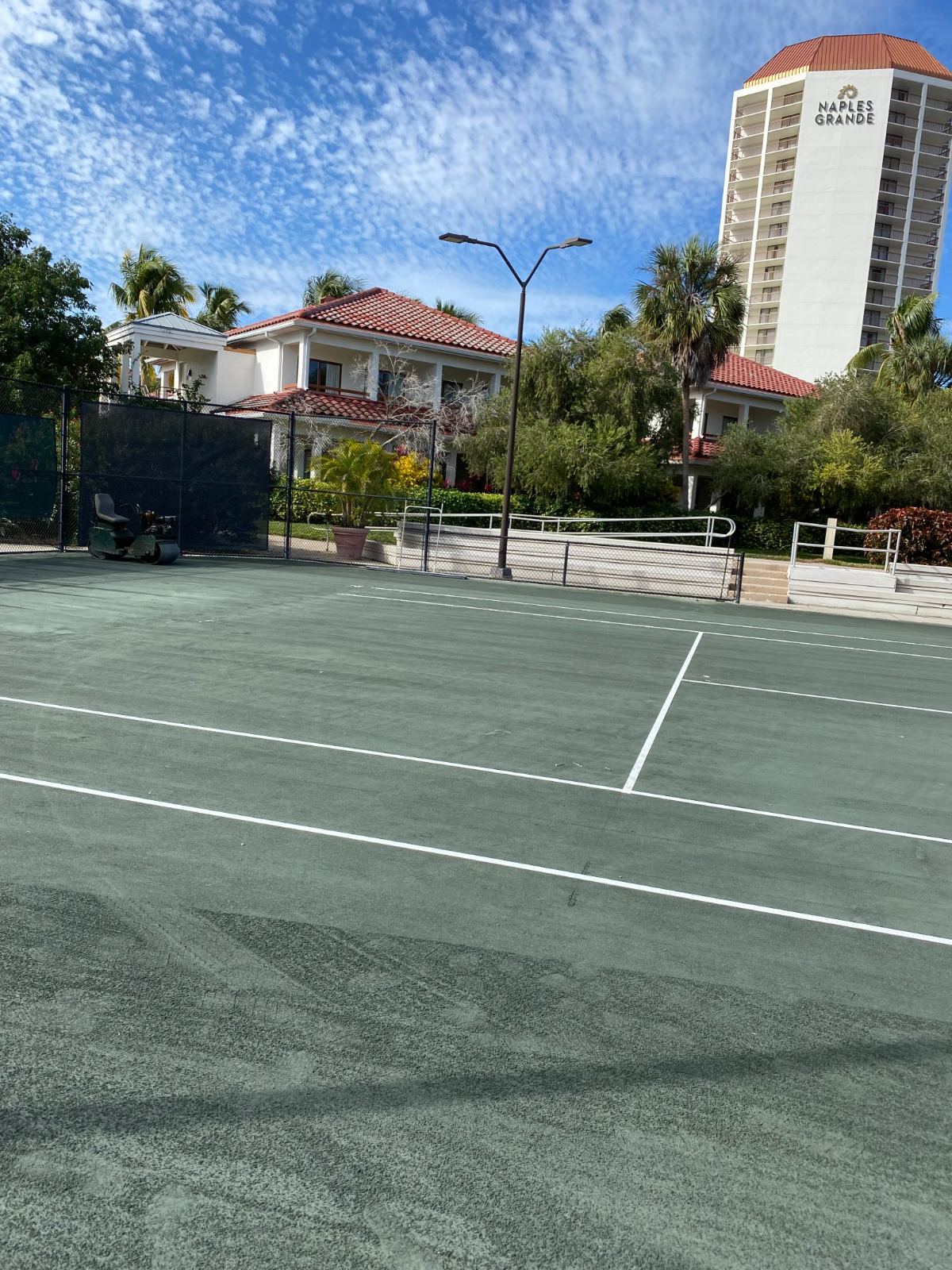 Tennis court at Naples Grande resort with red-roofed buildings and palm trees